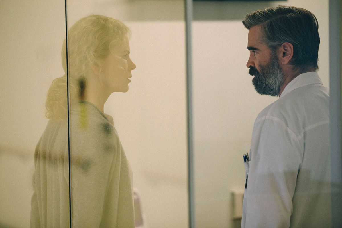 Steven (Colin Farrell), right, looks into a glass wall to his left. The reflection is that of his wife, Anna (played by Nicole Kidman).