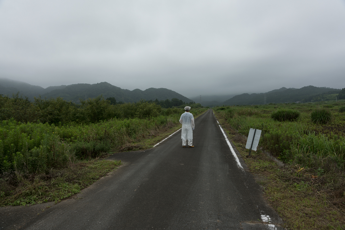 A man in a HAZMAT suit on an abandoned road