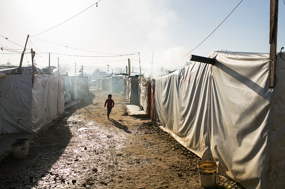 A boy runs between tents in the refugee camp in Beqaa Valley, Lebanon