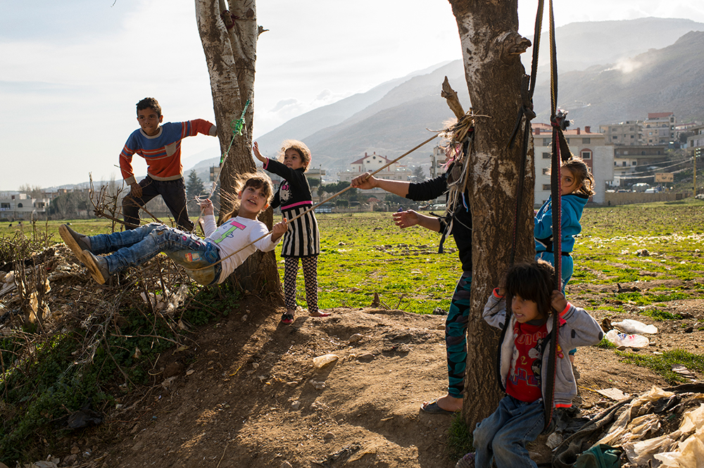 A group of young children play on a rope swing in the Beqaa valley refugee camp